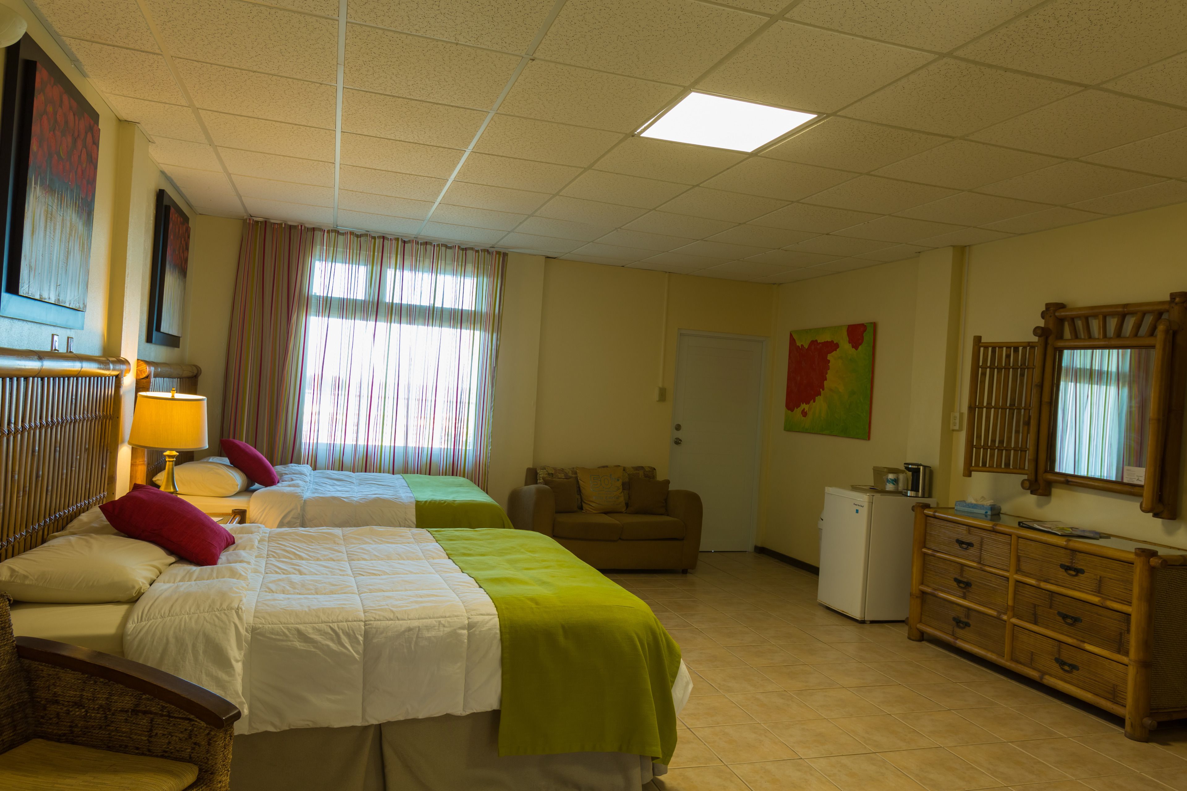A hotel room with two beds, a chair, a dresser, and a small refrigerator.
