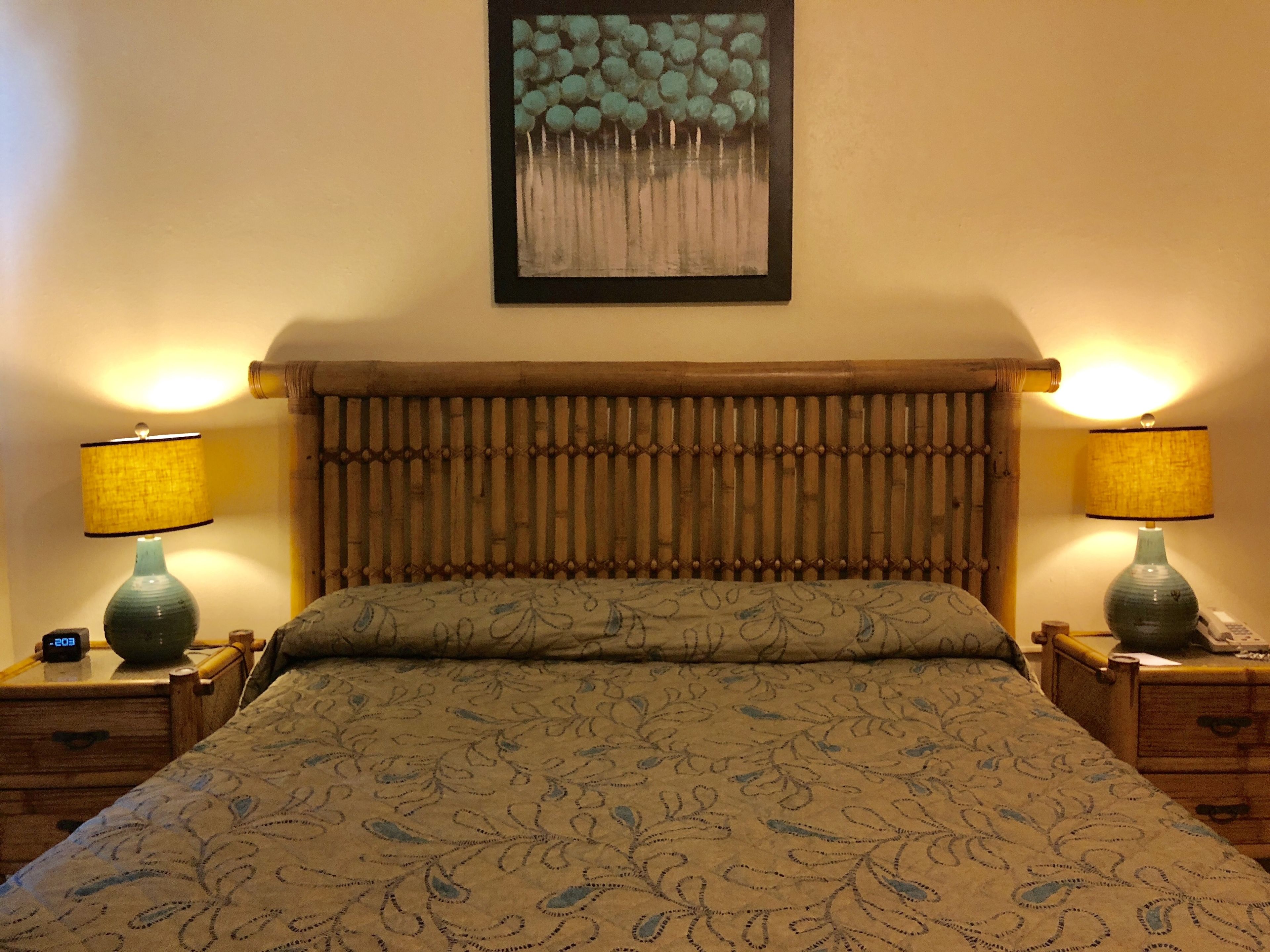 A bed with a patterned bedspread, two bedside tables with lamps, a wall-mounted painting, and a wooden headboard.