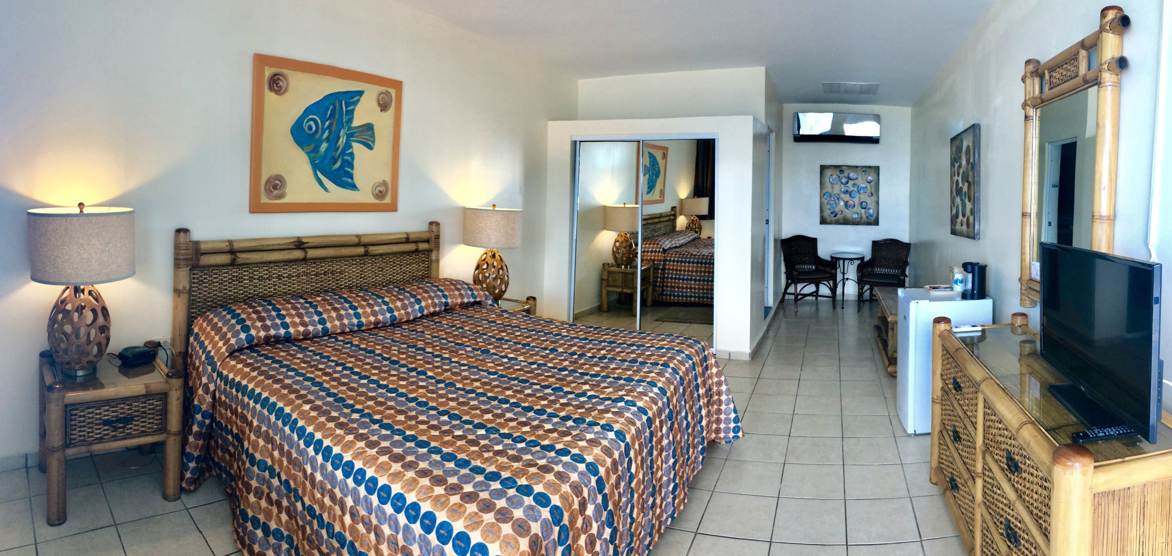 A hotel room with a large bed, a television, a desk with a computer, and a dining area with chairs and a table.