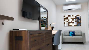 A modern office space with a wooden desk, a chair, a television mounted on the wall, and a sofa with a decorative pillow.