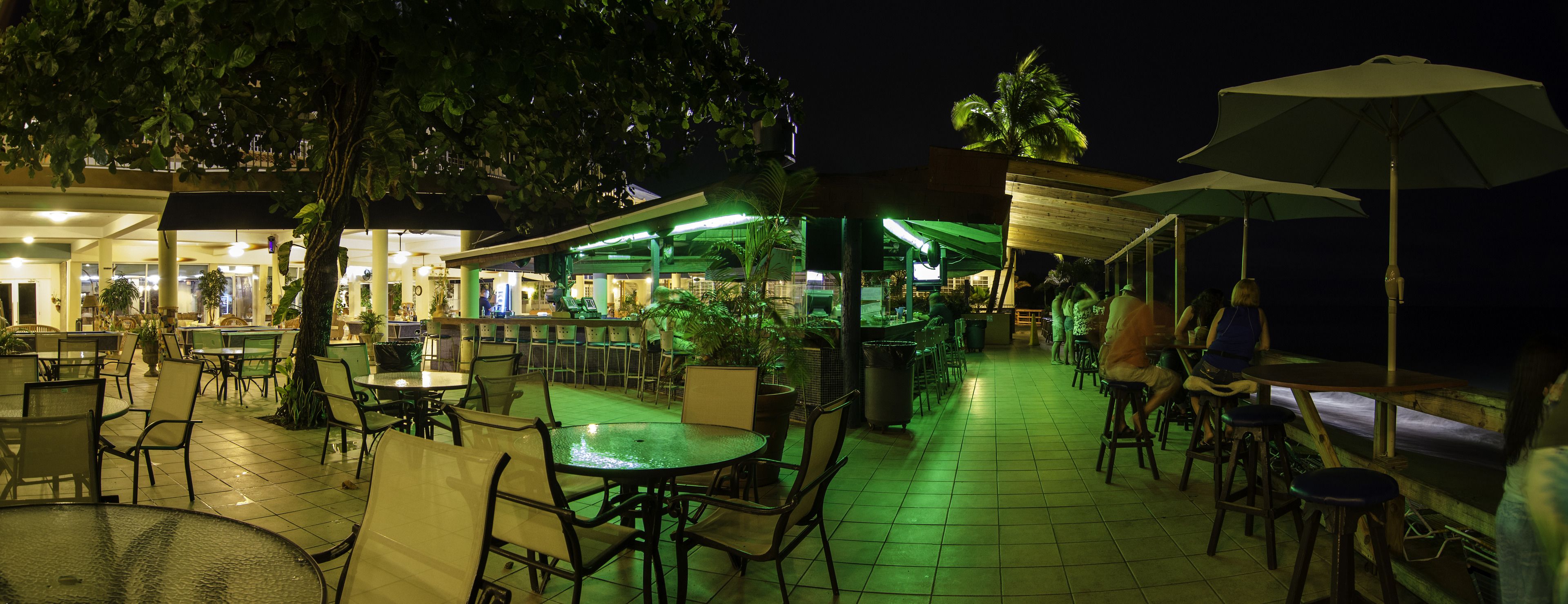 An outdoor dining area with tables and chairs, umbrellas, and a bar area with stools.