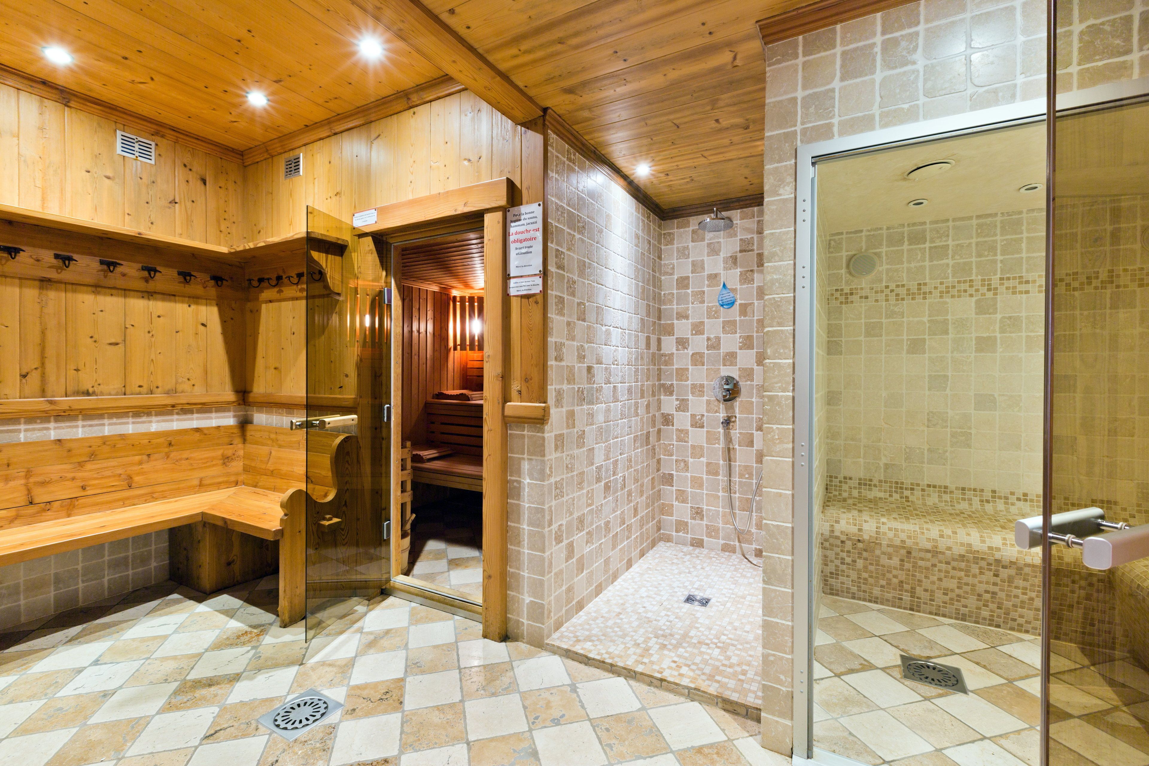 A sauna area with wooden benches, a glass door leading to a shower area with tiled walls.