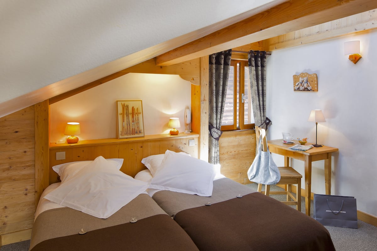 Une chambre confortable avec un plafond en bois, un lit avec une literie blanche et marron, une petite table avec une lampe et une fenêtre avec des rideaux.