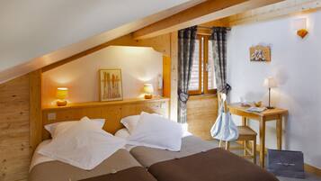 Un dormitorio acogedor con techo de madera, una cama con ropa de cama blanca y marrón, una mesita con lámpara y una ventana con cortinas.
