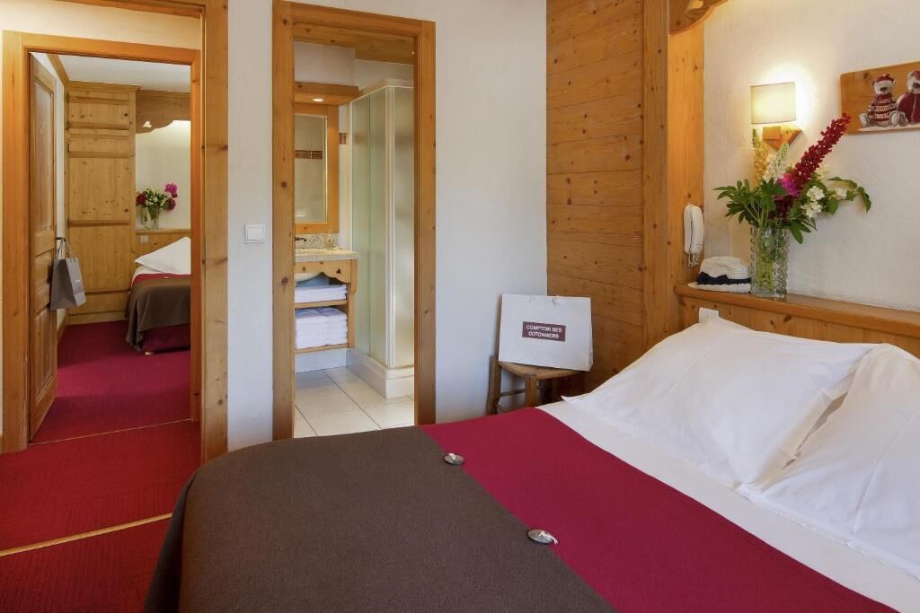 Habitación de hotel con cama, armario de madera, espejo, una mesita con un florero y alfombra roja.