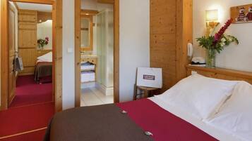 Habitación de hotel con cama, armario de madera, espejo, una mesita con un florero y alfombra roja.