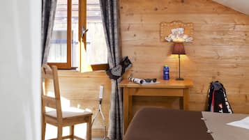 Una habitación de madera con una cama, un escritorio, una silla, una lámpara, una raqueta de tenis y una ventana con cortinas.