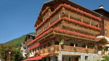 A hotel with multiple balconies adorned with flowers, outdoor seating, and a stone facade.
