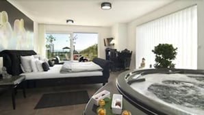 A modern hotel room with a large bed, a sitting area with a table, and a hot tub. - Burgunderhof Hotel - Adults Only (Hagnau)