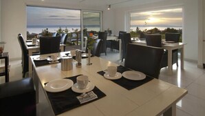A dining area with a view of the sea, featuring a long table with chairs, plates, and cups set for a meal. - Burgunderhof Hotel - Adults Only (Hagnau)