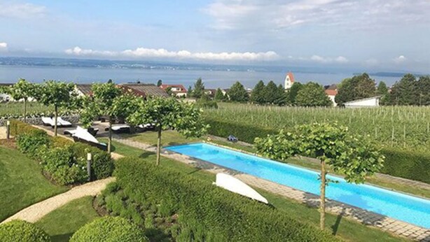 A swimming pool with a view of the sea and houses in the background. - Burgunderhof Hotel - Adults Only (Hagnau)