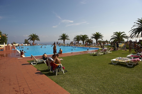 A pool area with multiple swimming pools, sun loungers, and palm trees.