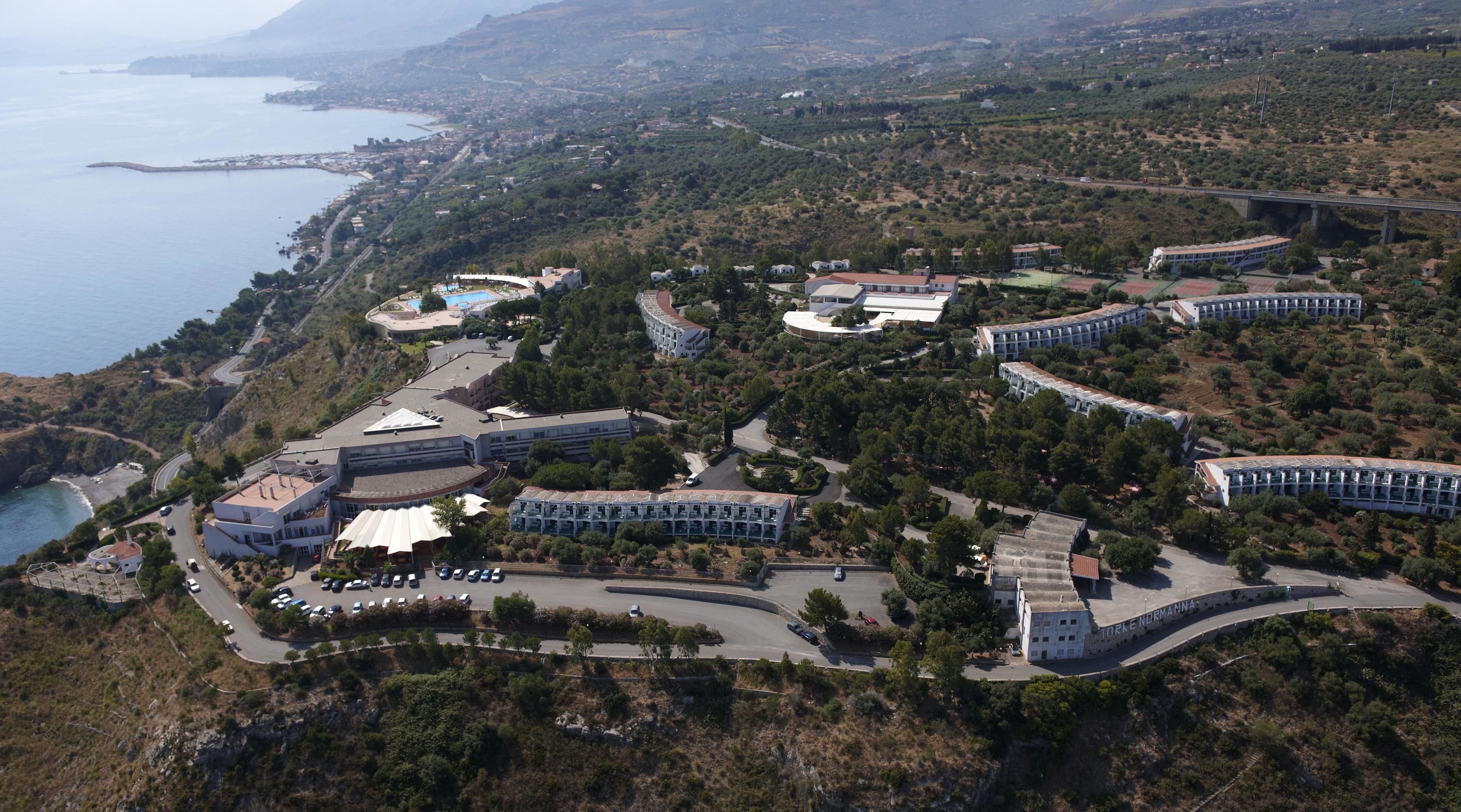 Vista aerea di un resort costiero con diversi edifici, un'area parcheggio e vista sul mare.