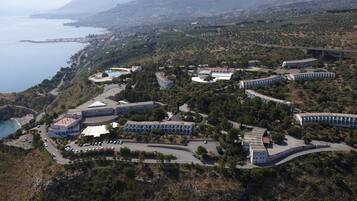Vista aerea di un resort costiero con diversi edifici, un'area parcheggio e vista sul mare.