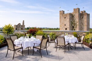 Una terraza con mesas dispuestas para comer, con vistas a un castillo histórico.