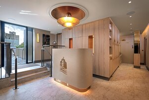 Zona de recepción de hotel con diseño moderno, que incluye un mostrador de recepción, una escalera y vistas a un castillo a través de puertas de cristal.