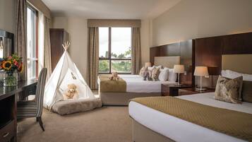 A hotel room with two beds, a desk, a chair, a TV, a window with curtains, and a teddy bear in a teepee.