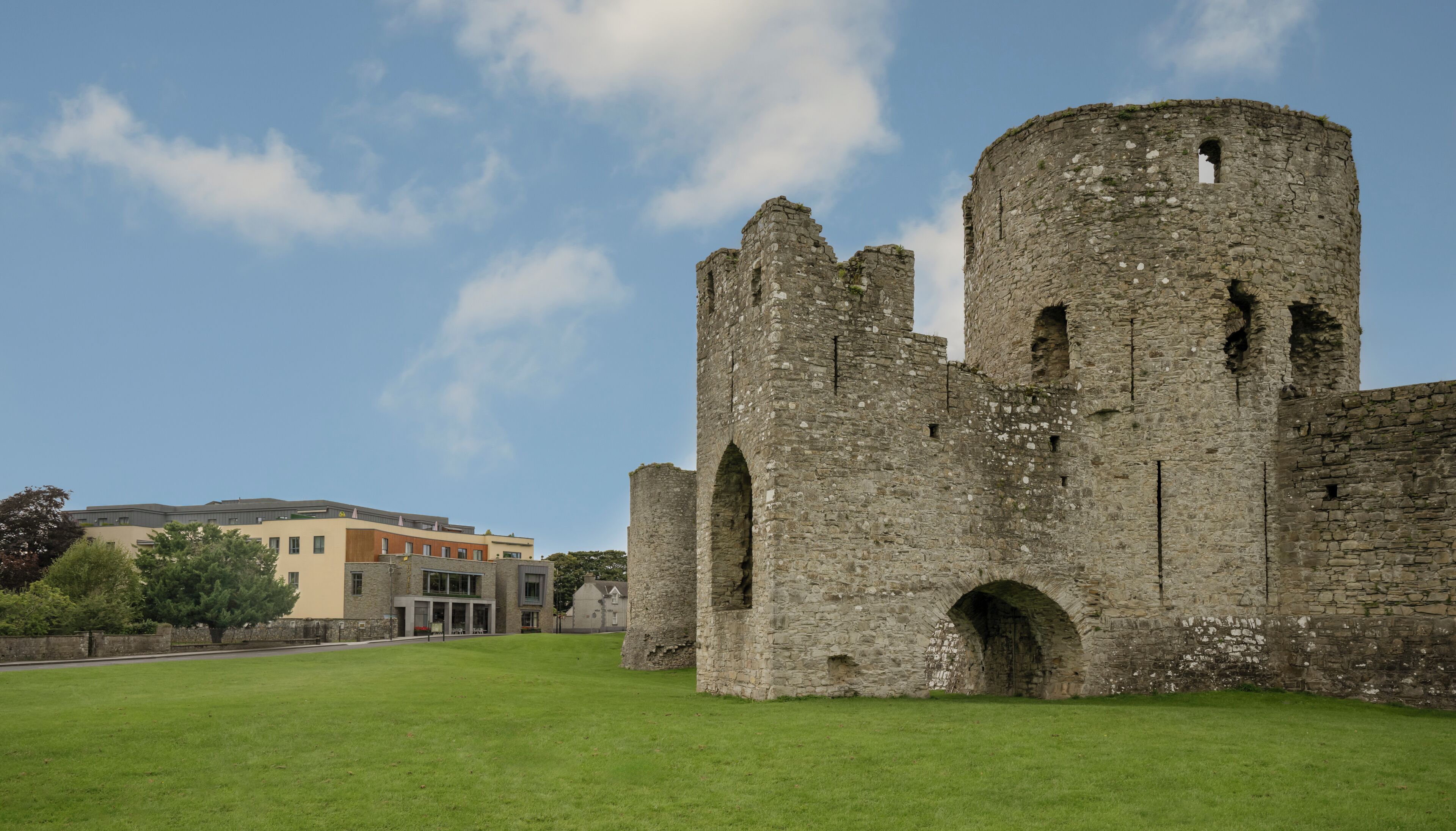 A historic stone castle with arched windows and a round tower, surrounded by a well-maintained lawn.