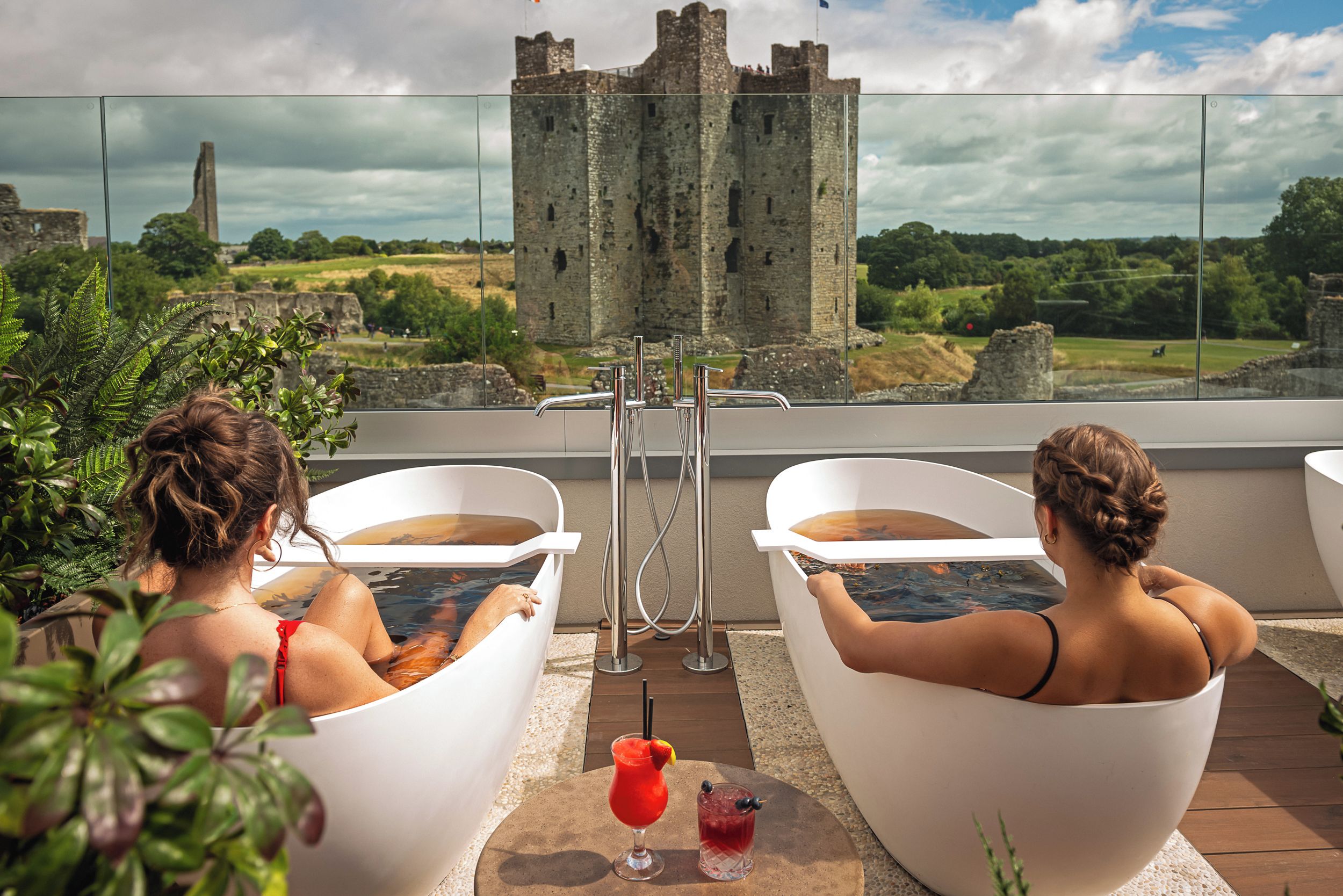Two individuals relaxing in white tubs with a castle in the background.