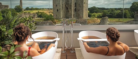 Two individuals relaxing in white tubs with a castle in the background.