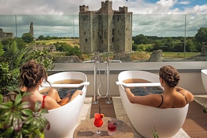 Dos personas descansando en tinas blancas, con un castillo al fondo.