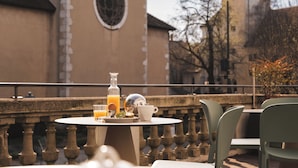 Uma mesa com itens de café da manhã, uma garrafa e uma xícara, com uma igreja e árvores ao fundo.