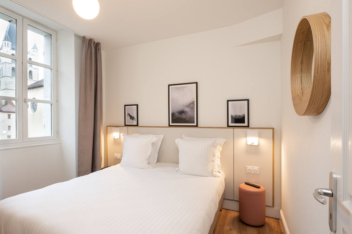 A hotel room with a large bed, a window with curtains, a wall-mounted wooden piece, and framed pictures.