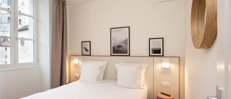 A hotel room with a large bed, a window with curtains, a wall-mounted wooden piece, and framed pictures.