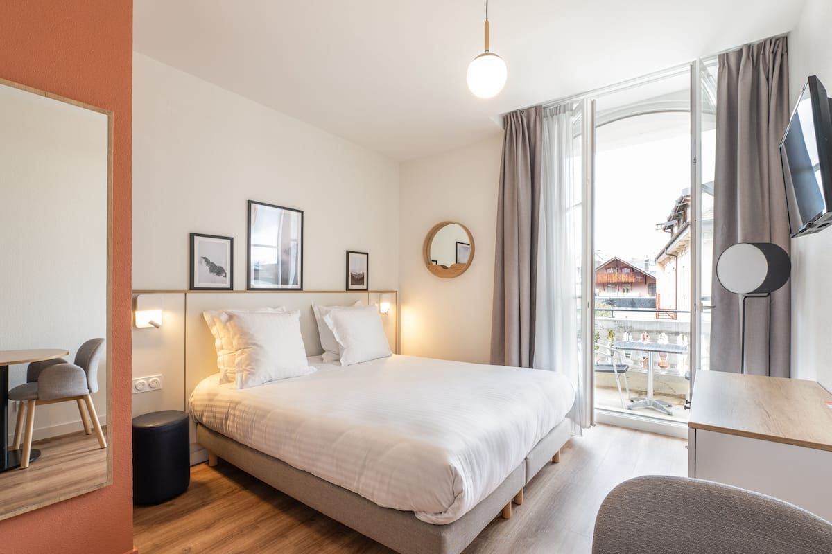 A hotel room with a bed, bedside table, chair, and a view of the outside.