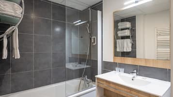 A modern bathroom with a glass-enclosed shower, a white bathtub, and a wooden vanity with a sink.
