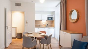 Una cucina moderna con mobili bianchi, un forno a microonde e un lavello. C'è un'area pranzo con un tavolo rotondo e sedie.