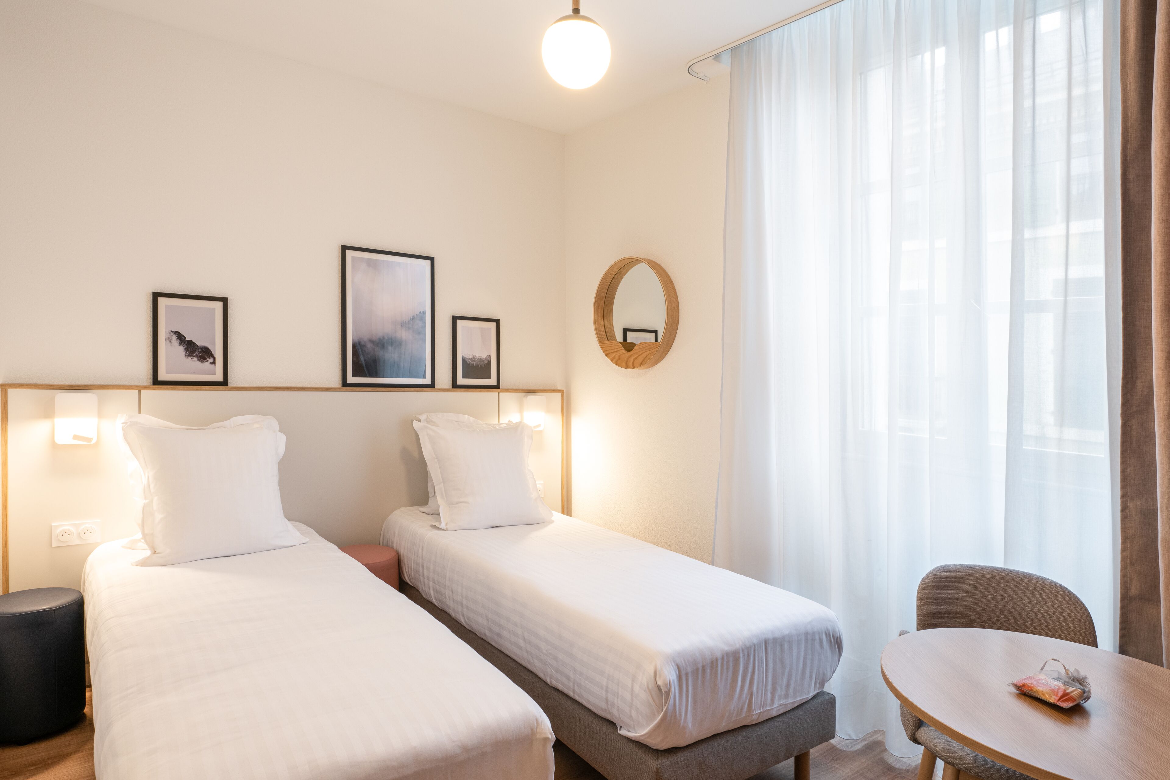 Hotellihuoneessa on kaksi erillistä sänkyä, pyöreä pöytä ja tuoli. Seinälle on asennettu valaisimet, ja sänkyjen yläpuolella on peili.