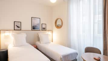 Een hotelkamer met twee enkele bedden, een ronde tafel en een stoel. Er zijn wandlampen en een spiegel boven de bedden.