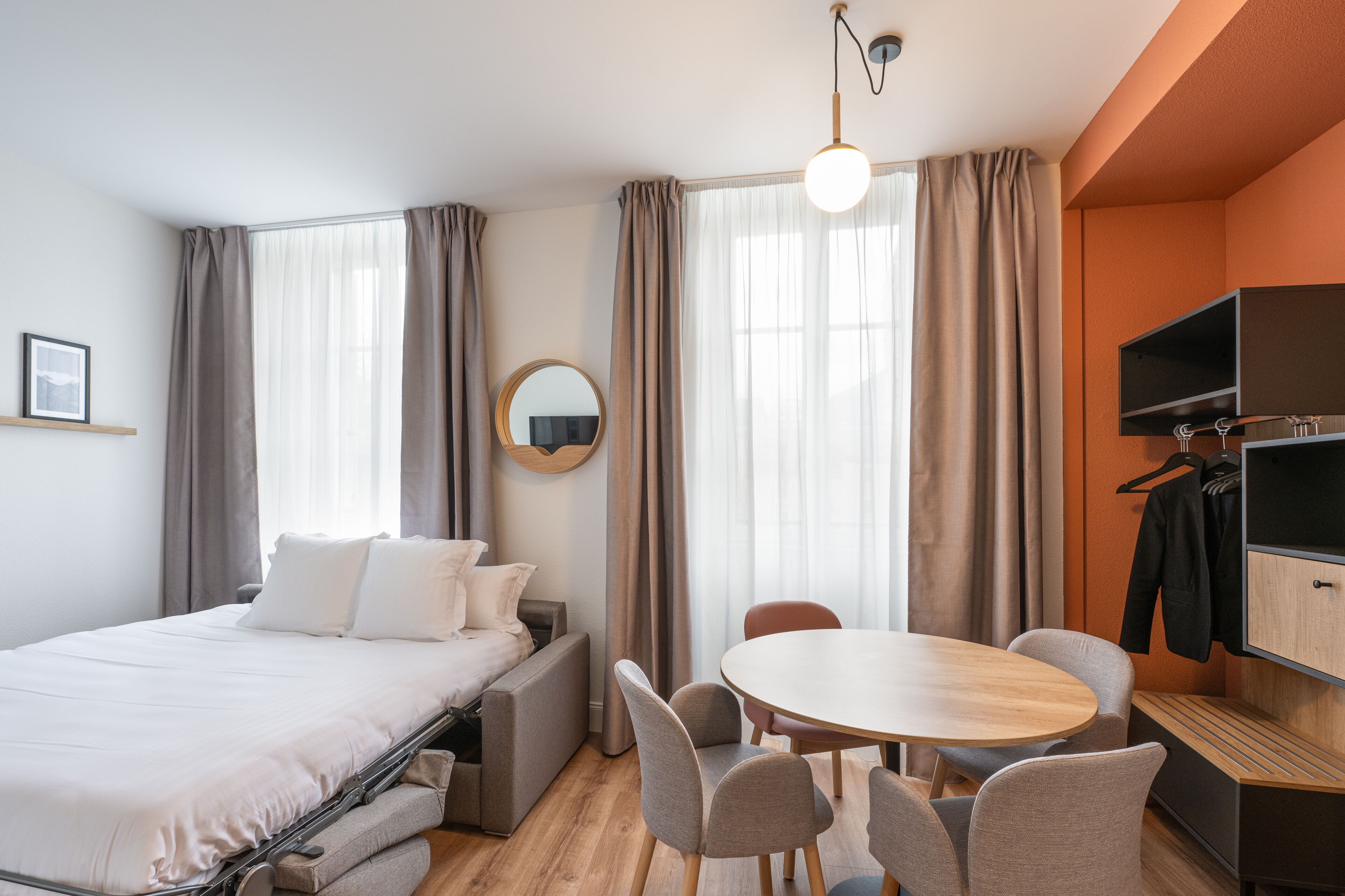 A hotel room with a bed, a round table, and chairs, a TV, and a coat rack.