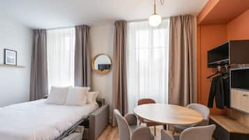 A hotel room with a bed, a round table, and chairs, a TV, and a coat rack.