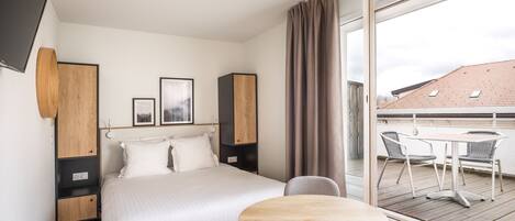 Una habitación de hotel moderna con una cama grande, una mesa redonda de madera y un balcón con mesa y sillas.