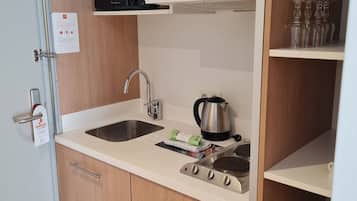 A compact kitchen with a microwave, kettle, and stove. There are wooden cabinets and a sink.