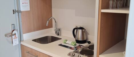 A compact kitchen with a microwave, kettle, and stove. There are wooden cabinets and a sink.