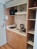 Kompakti keittiö, jossa on mikroaaltouuni, vedenkeitin ja liesi. Keittiössä on puukaapit ja pesuallas.