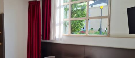 Ein Zimmer mit Fenster, einem roten Tisch, zwei Stühlen und einem Bett.