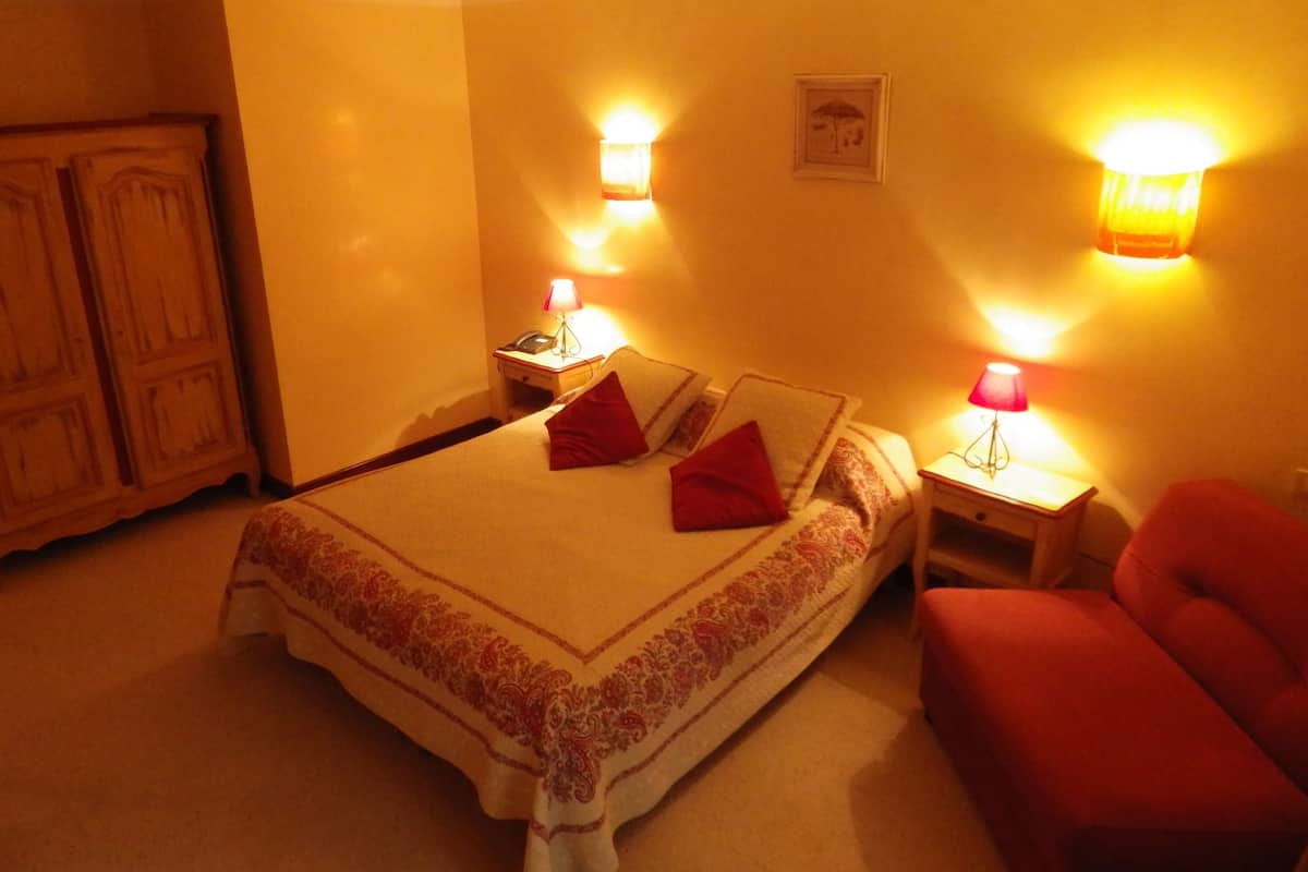A hotel room with a bed, two bedside tables with lamps, a red chair, and a wardrobe.
