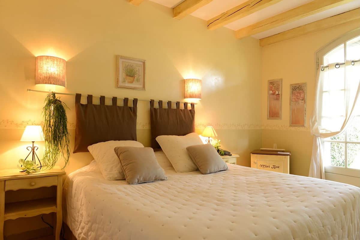 A cozy bedroom with a large bed, two bedside lamps, a nightstand, and a window with curtains.