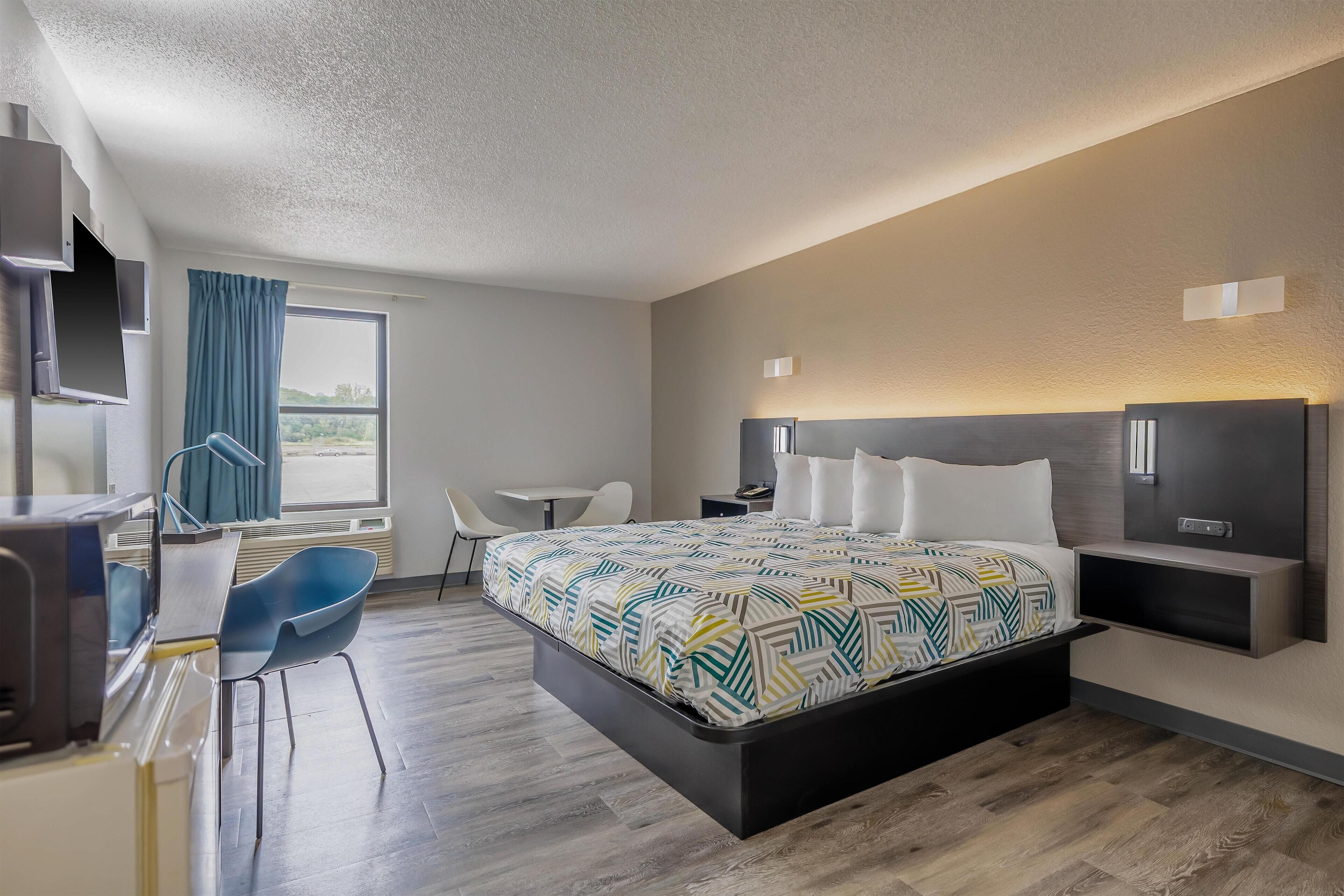 A modern hotel room with a large bed, a desk with a chair, a TV, and a window with curtains.