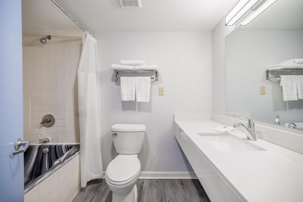 Un baño moderno con inodoro blanco, bañera con cortina de ducha, tocador con espejo y un perchero para toallas.