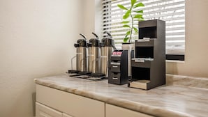 A coffee station with multiple kettles, a tea dispenser, and a shelf with a plant. - Motel 6 Franklin, OH (Franklin)