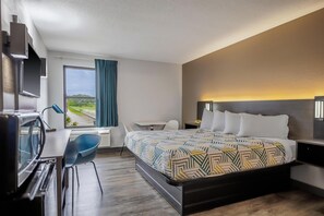 A modern hotel room with a bed, desk, and chair, a TV, and a large window with a view.