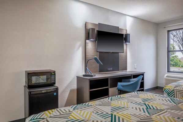 A hotel room with a bed, a desk with a chair, a microwave, and a television.