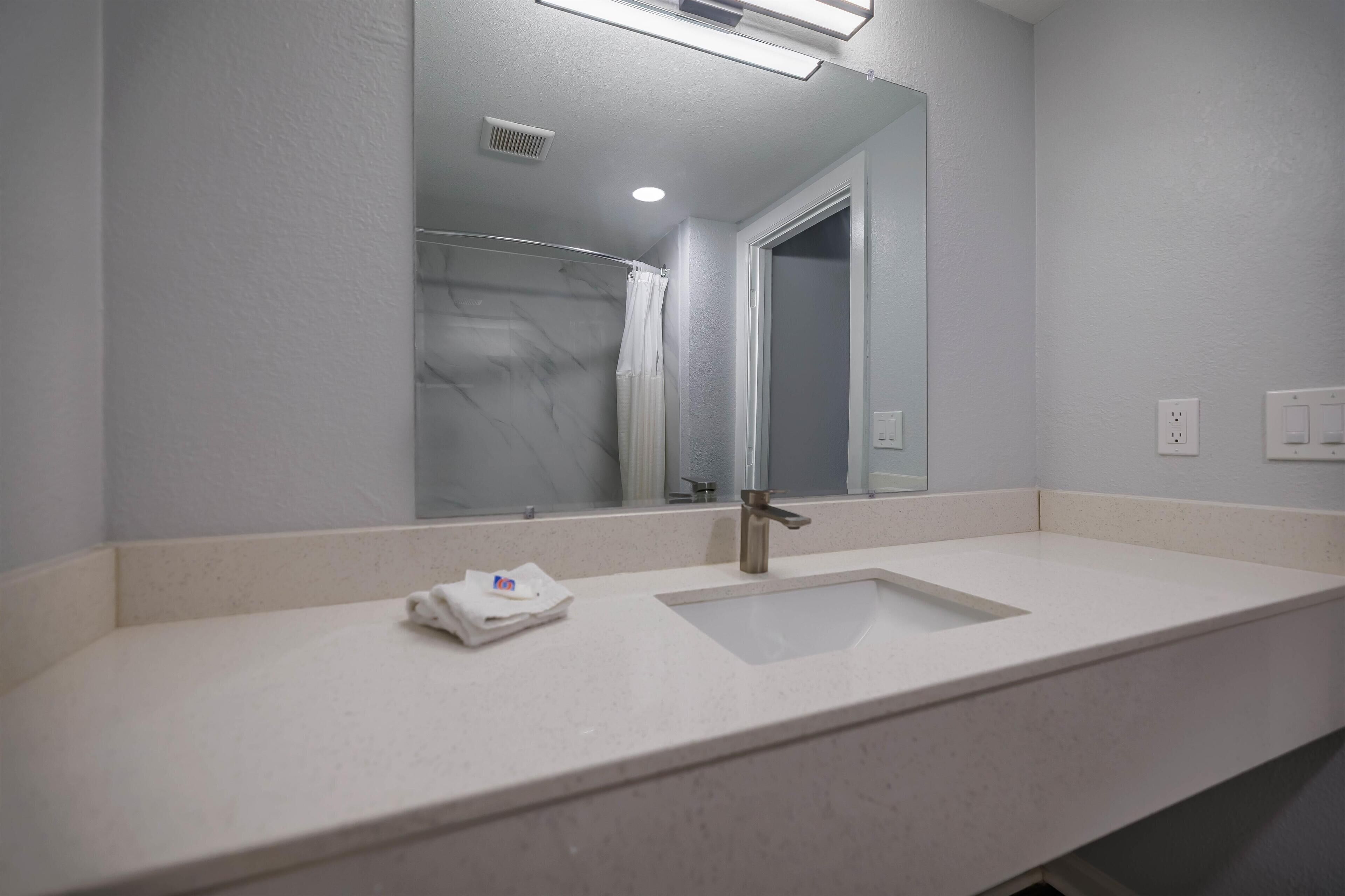 A bathroom with a large mirror, two sinks, and a shower visible in the reflection.