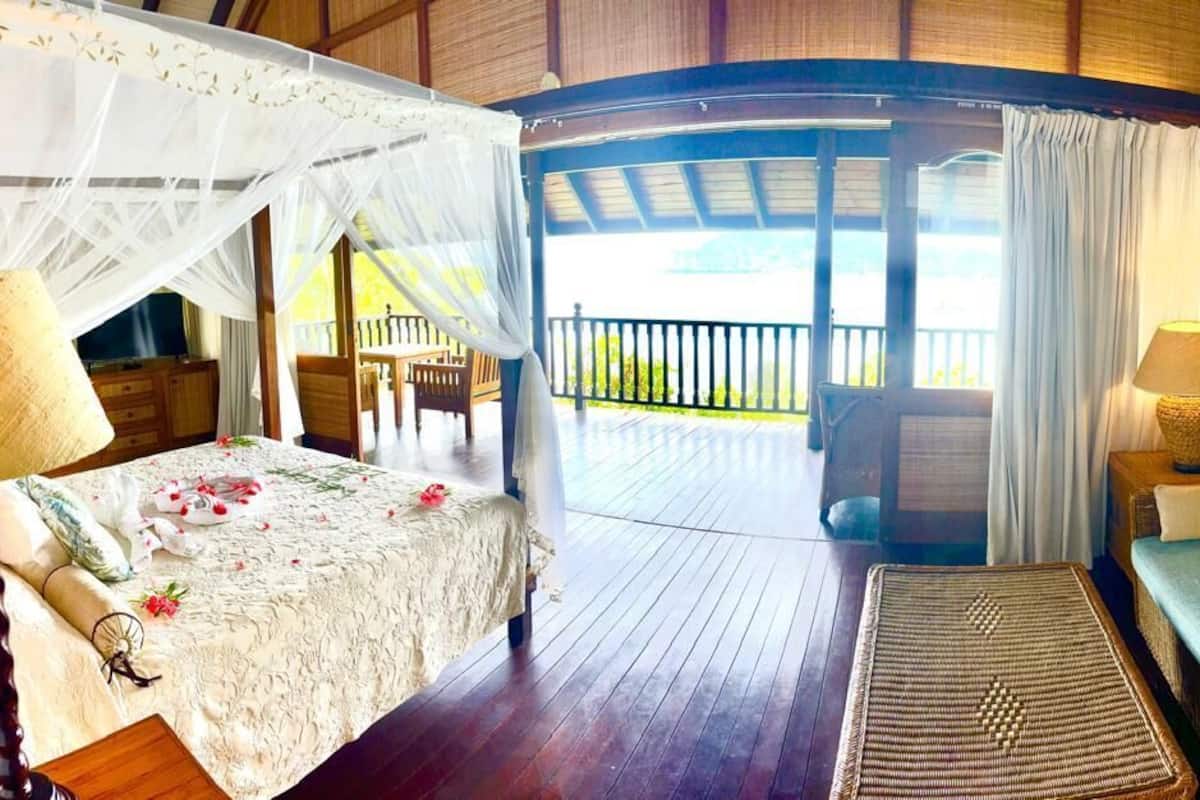 A room with a bed, a sofa, a table, and a balcony with a view.