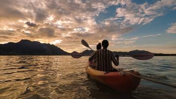 Una pareja en un kayak rojo sobre aguas tranquilas, con montañas al fondo y un cielo nublado.